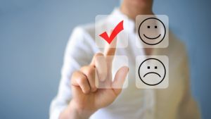 A stock image of a person selecting a happy face icon over a sad face icon